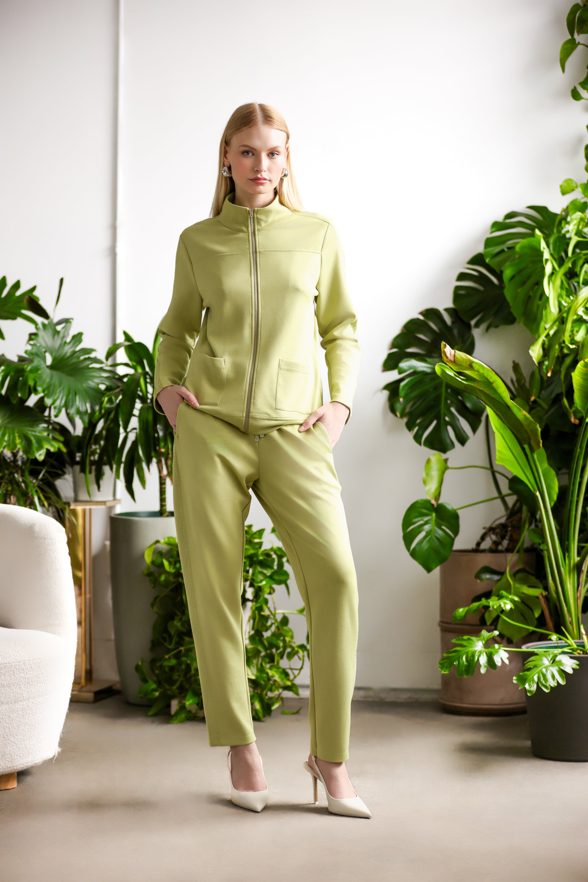 Women’s zip-front cardigan top with a structured silhouette and matching slim-fit pants, shown on a model standing indoors with natural light and greenery.