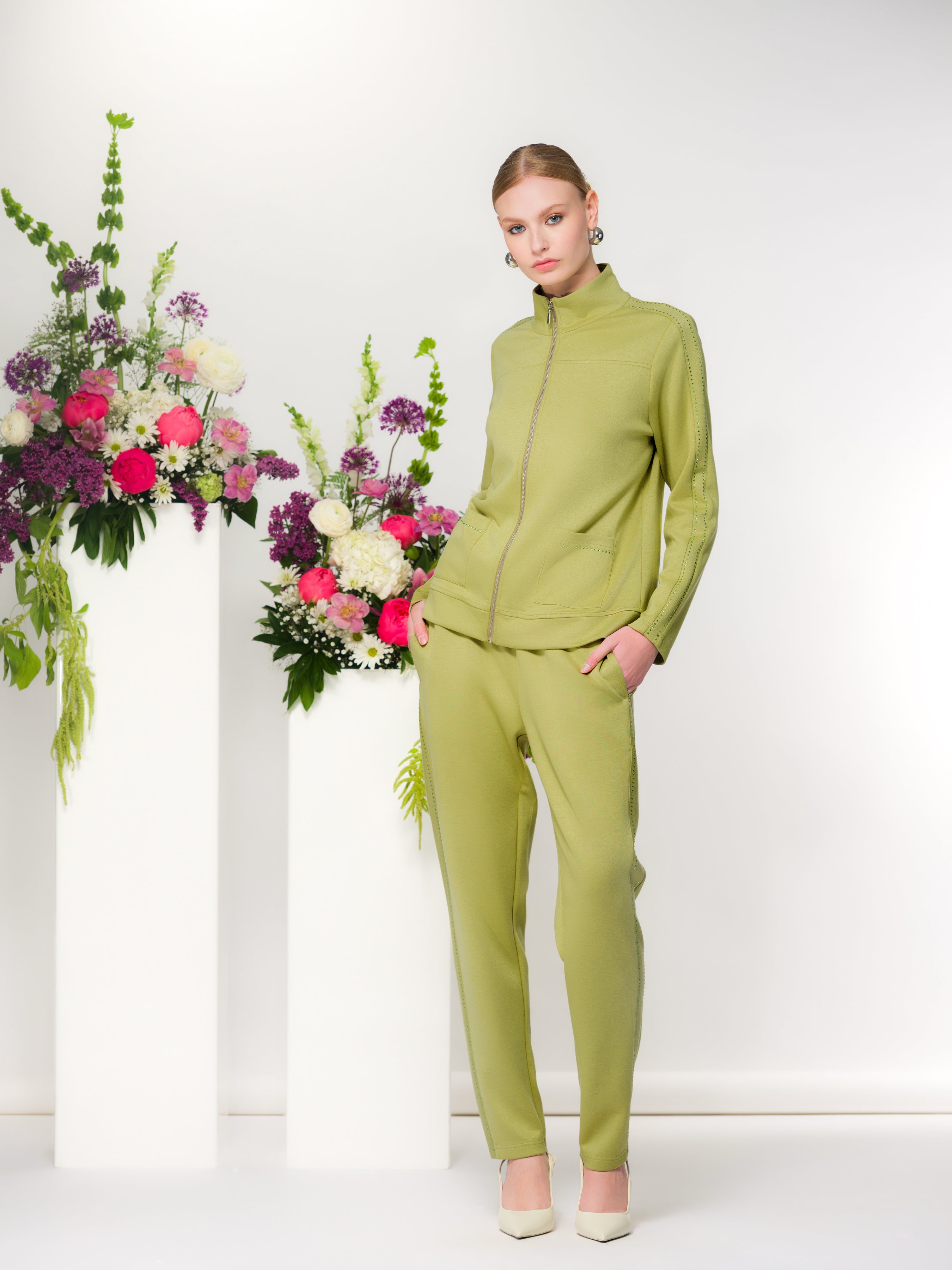 Women’s zip-front cardigan top with a structured silhouette and matching slim-fit pants, shown on a model standing indoors with natural light and florals.