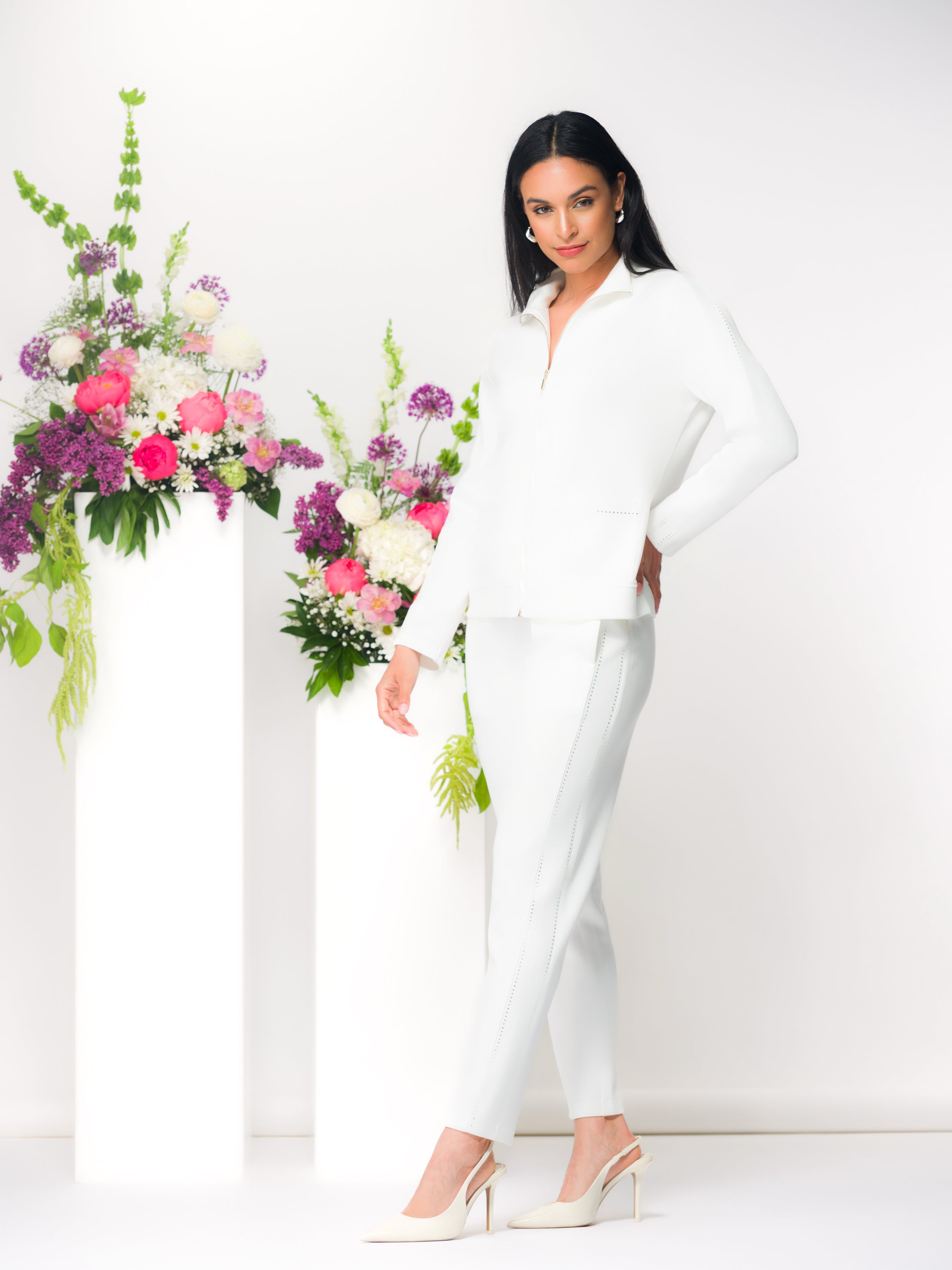 Women’s zip-front cardigan top with a structured silhouette and matching slim-fit pants, shown on a model standing indoors with natural light and florals.