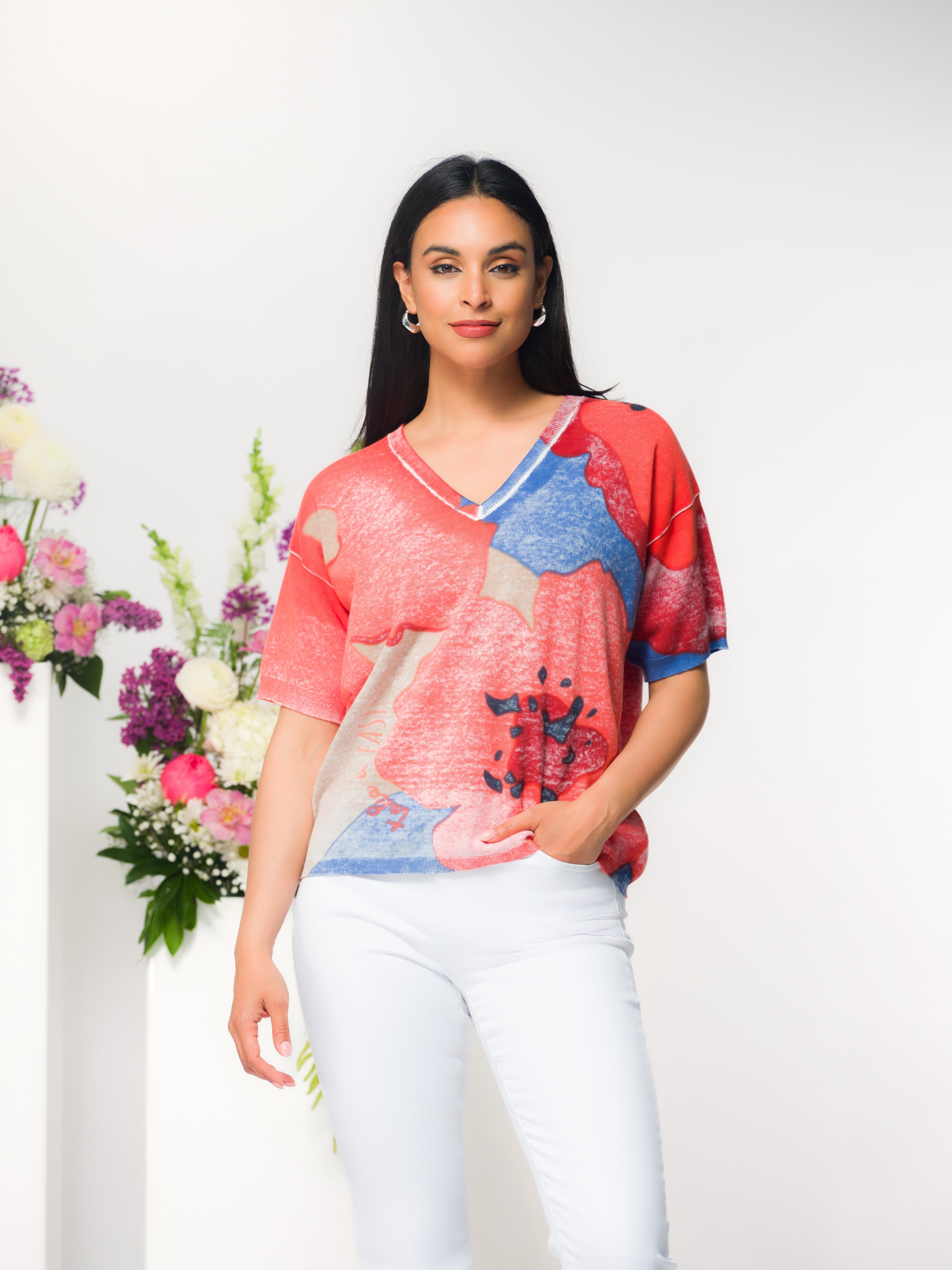 Woman wearing a relaxed-fit V-neck cotton sweater with an abstract print, styled with slim-fit pants, shown on a studio model.