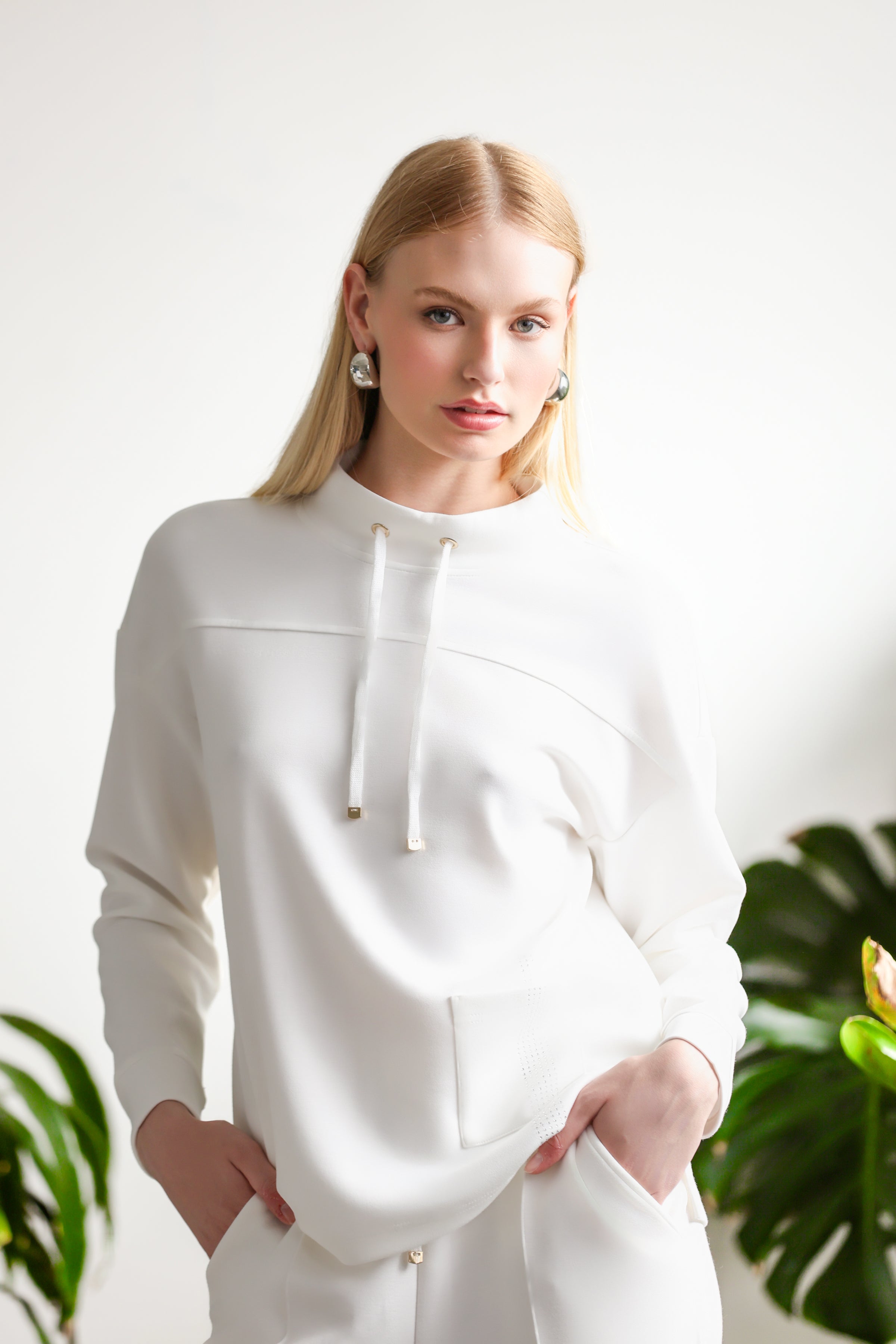 Model wearing a soft-drape pullover with a relaxed silhouette, photographed in a minimalist studio surrounded by indoor plants.
