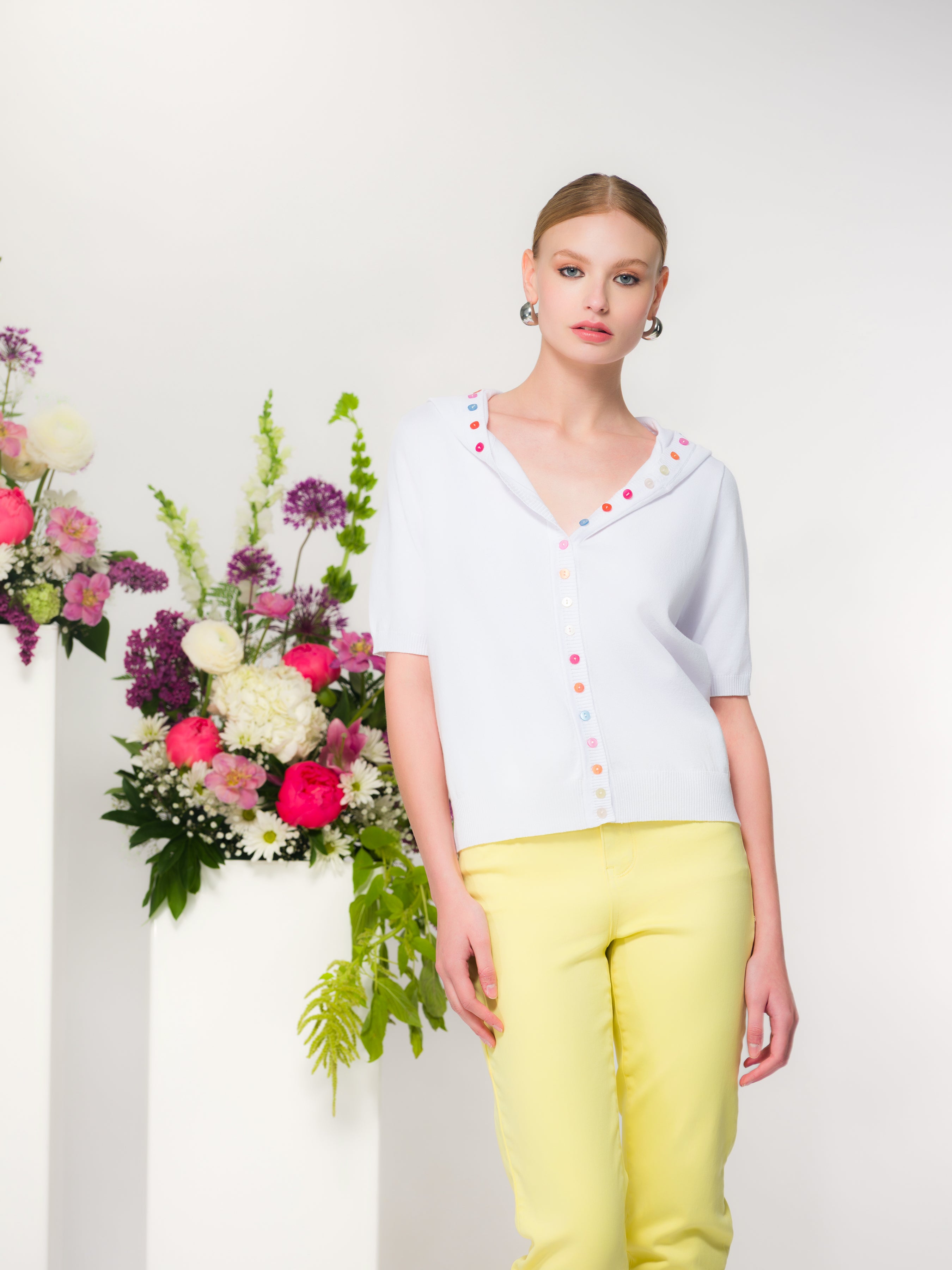 Model wearing a soft lavender short-sleeve hooded cardigan with multicolour button-front detail, paired with pastel yellow pants.