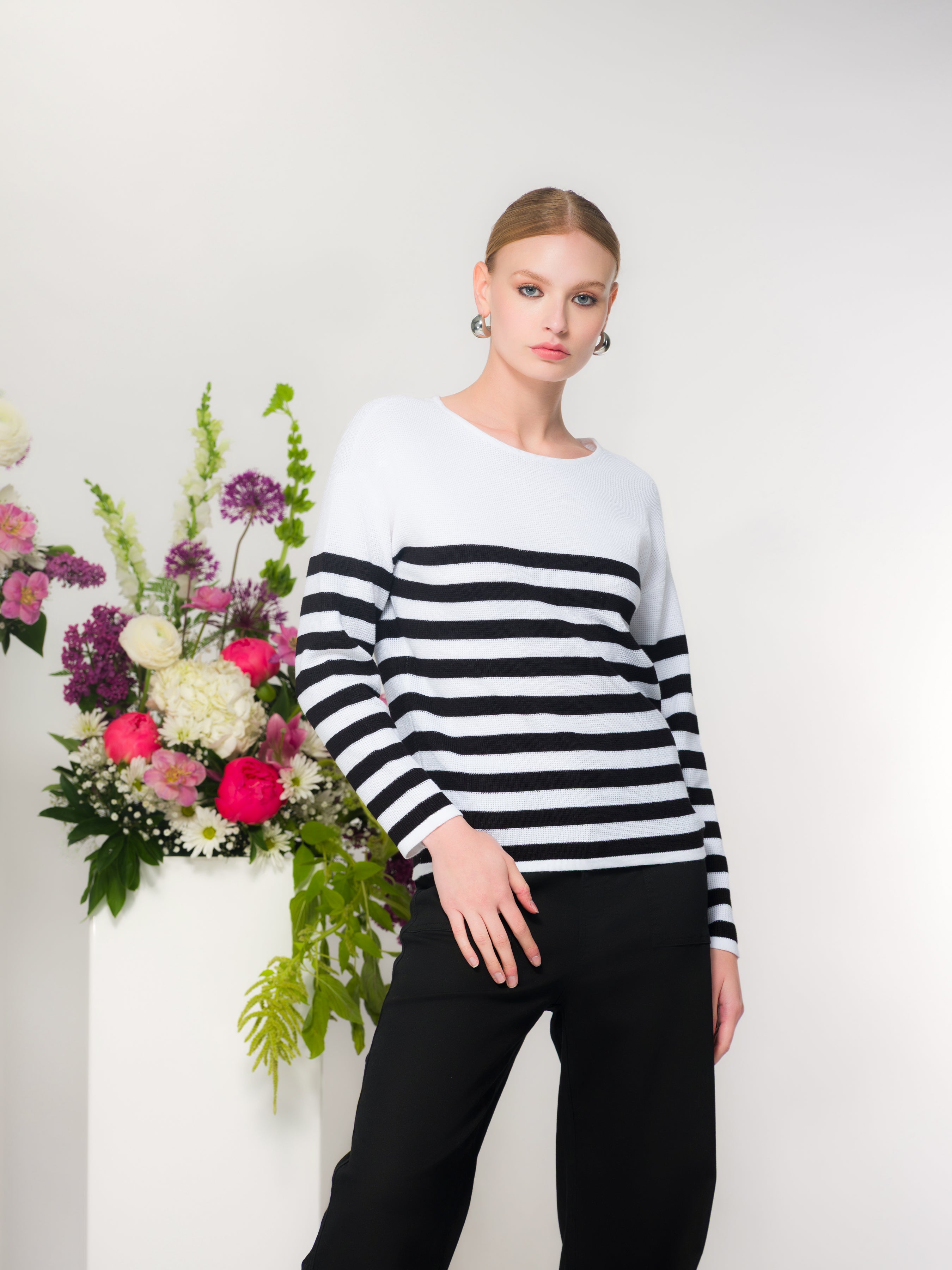 Women’s lightweight knit sweater in white with black horizontal stripes, long sleeves and classic crew neck, paired with black trousers.