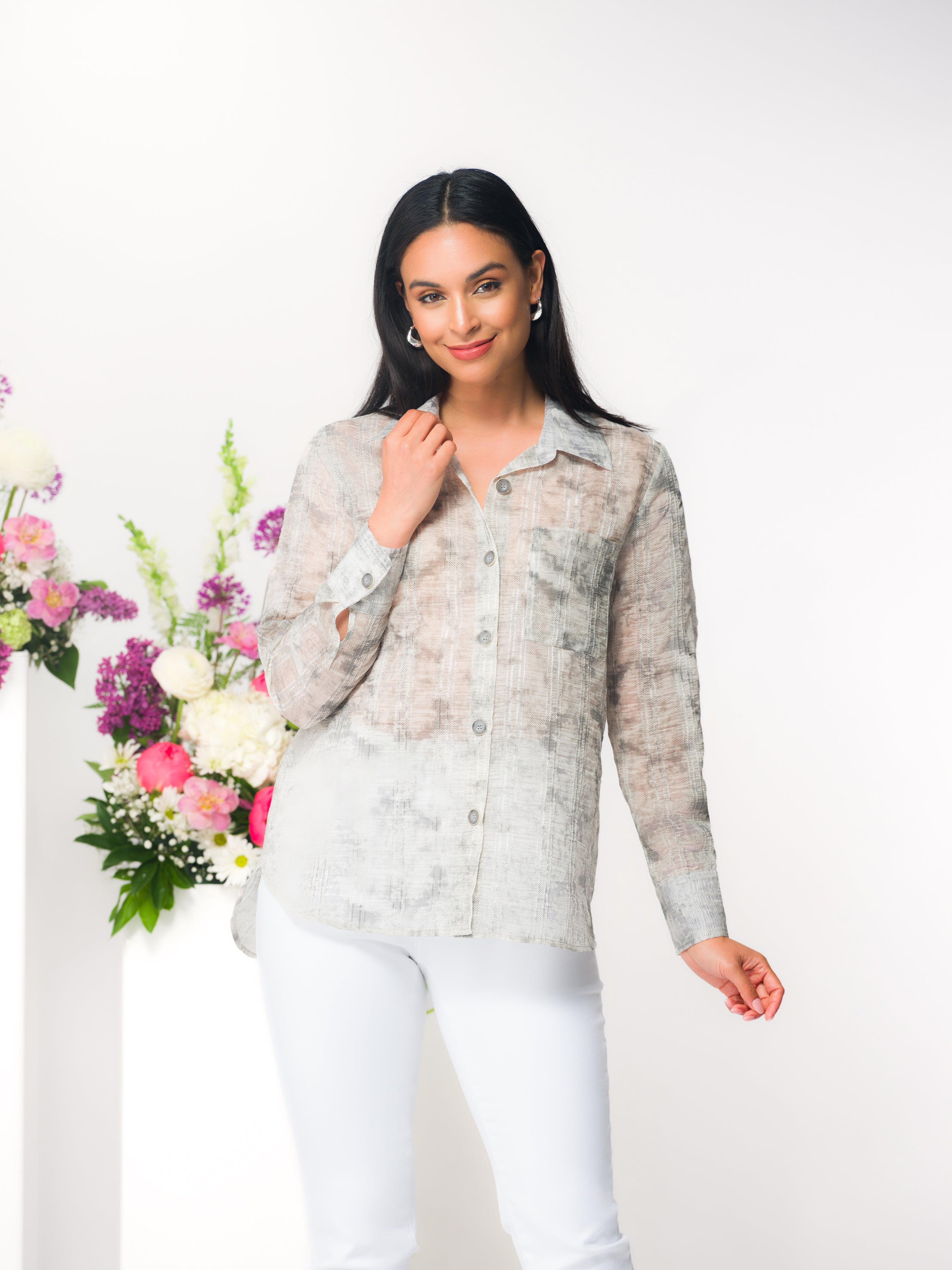 Woman wearing a lightweight abstract print button-up blouse in soft neutral tones with long sleeves and a relaxed fit, paired with slim light grey pants.