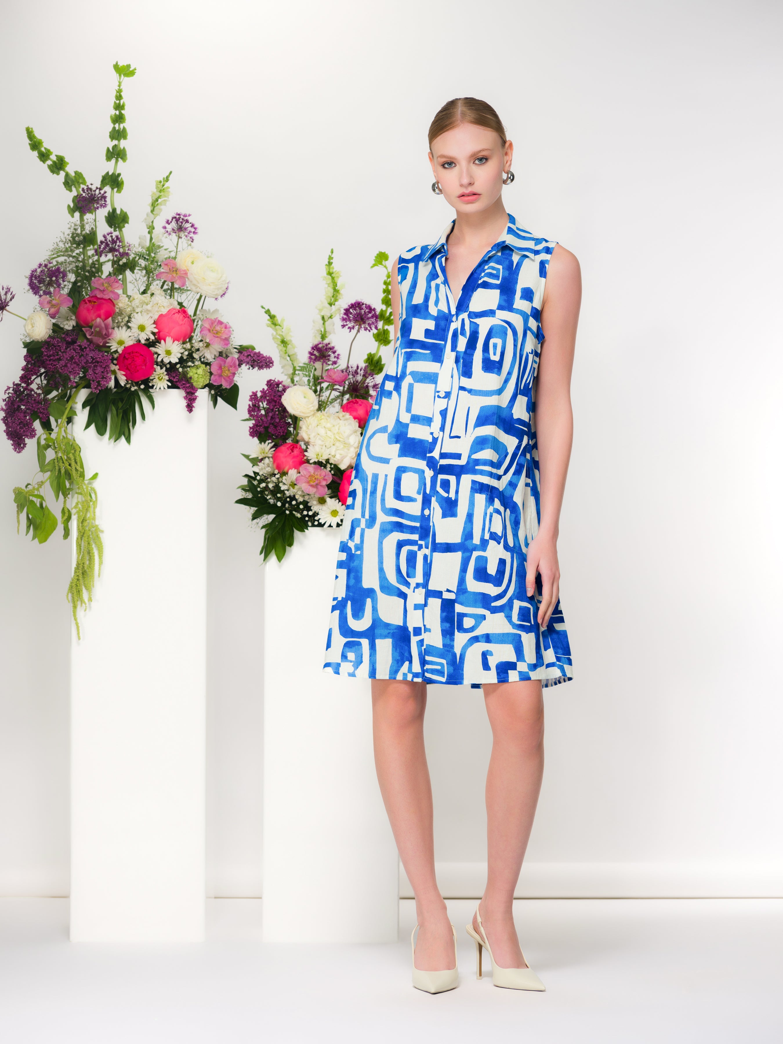 Front view of a sleeveless blue and white geometric print linen blend shirt dress with button-front detail, worn with cream slingback heels.