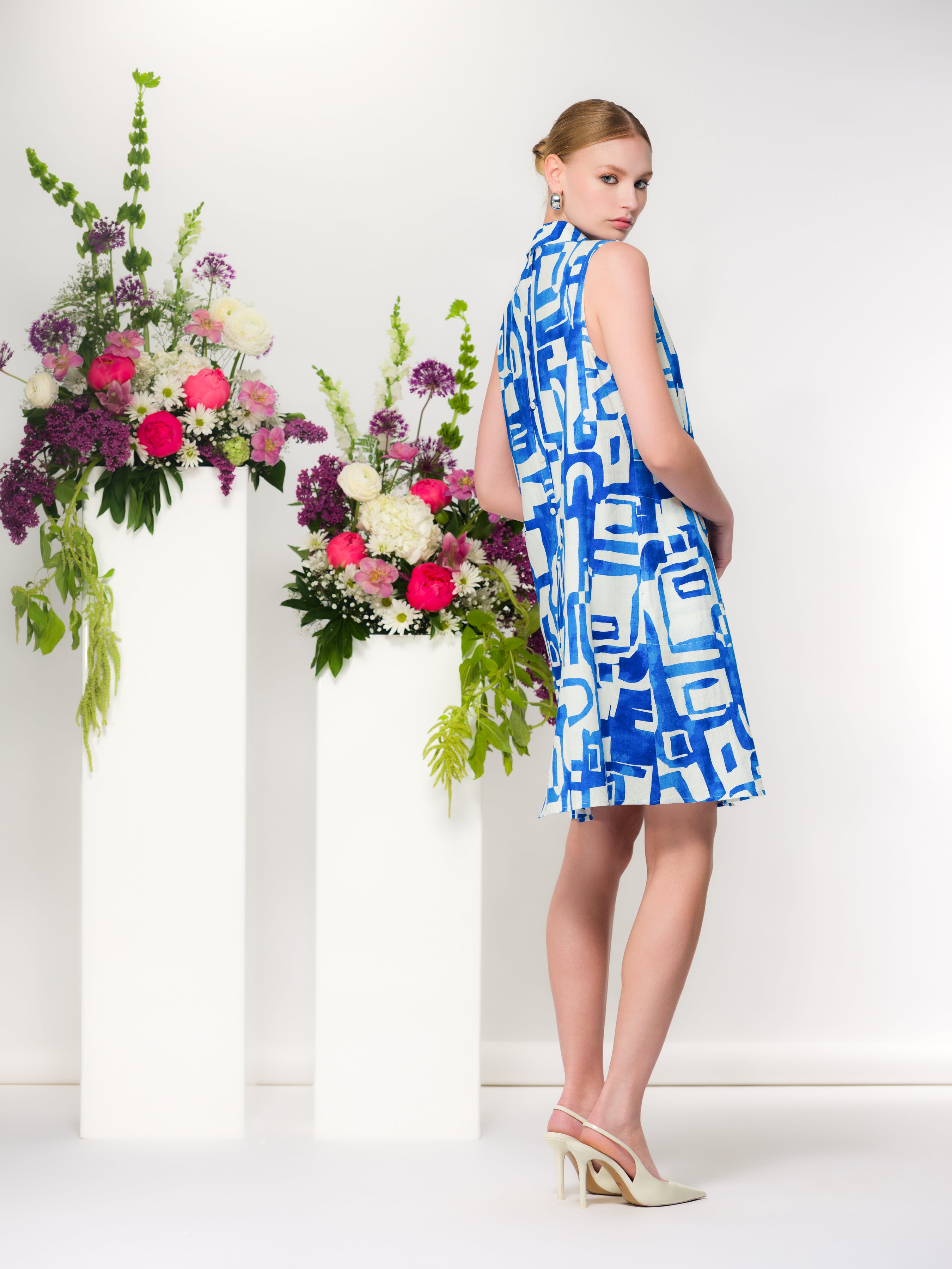 Back and side view of a sleeveless blue and white geometric print linen blend shirt dress with relaxed A-line silhouette, styled with cream slingback heels.