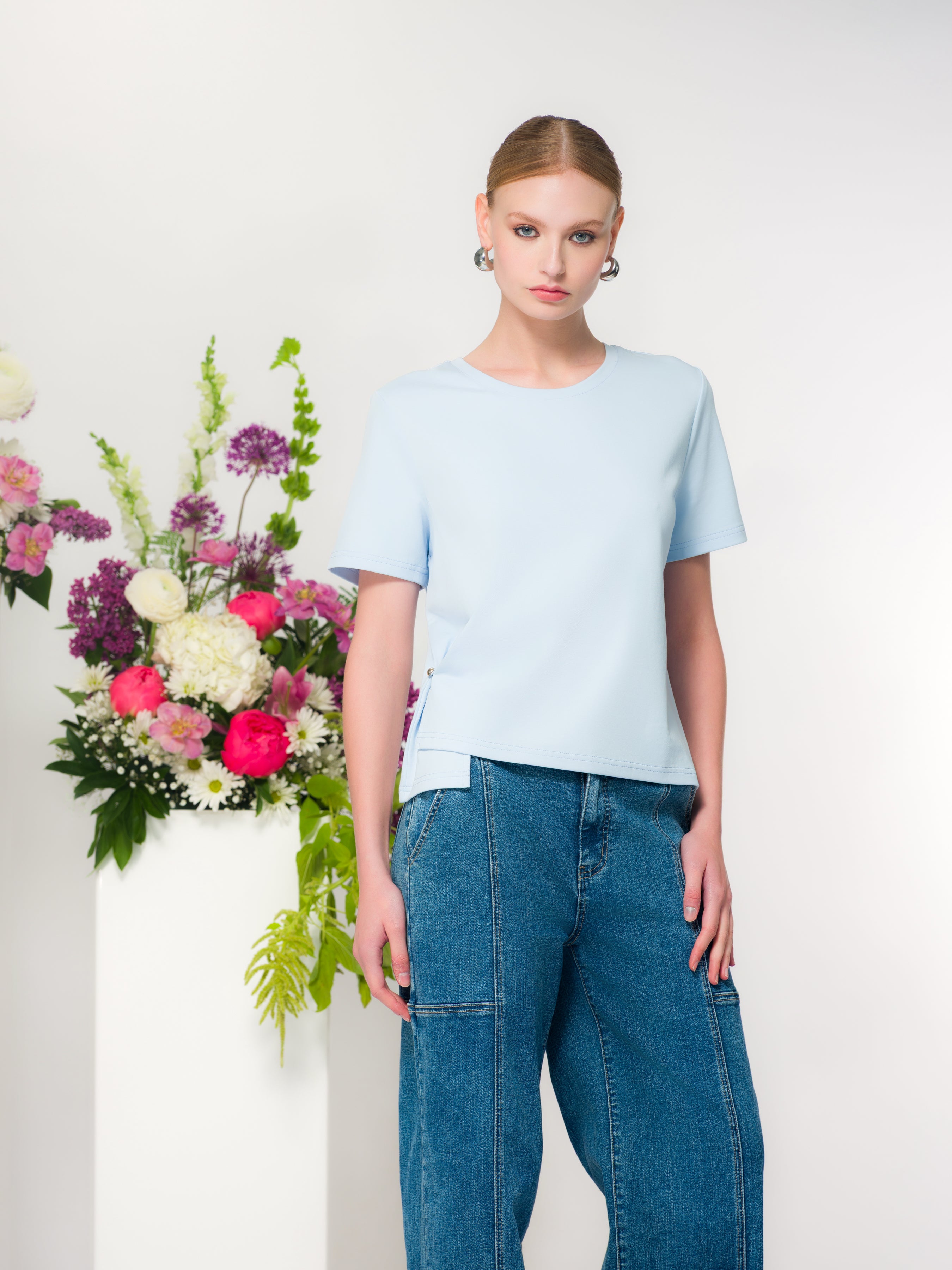 Women’s light blue relaxed-fit crew neck t-shirt with short sleeves and side slit detail, styled with blue denim jeans.