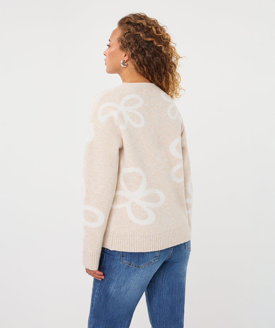 Back biew of a woman wearing a beige patterned crew-neck sweater, highlighting the knit texture, abstract motif, ribbed neckline, and cuffs.