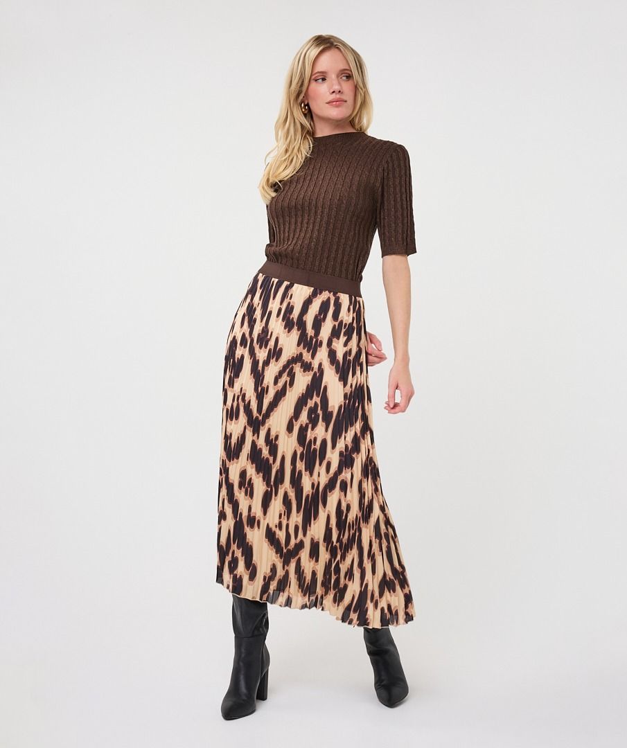 Woman modelling a brown ribbed knit short-sleeve top with a high neckline and fitted silhouette, paired with a printed skirt and black boots.