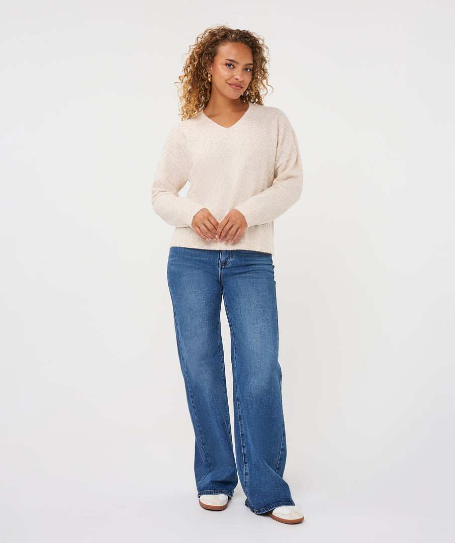 Woman wearing an ivory V-neck sweater with long sleeves and a relaxed fit, paired with blue jeans.