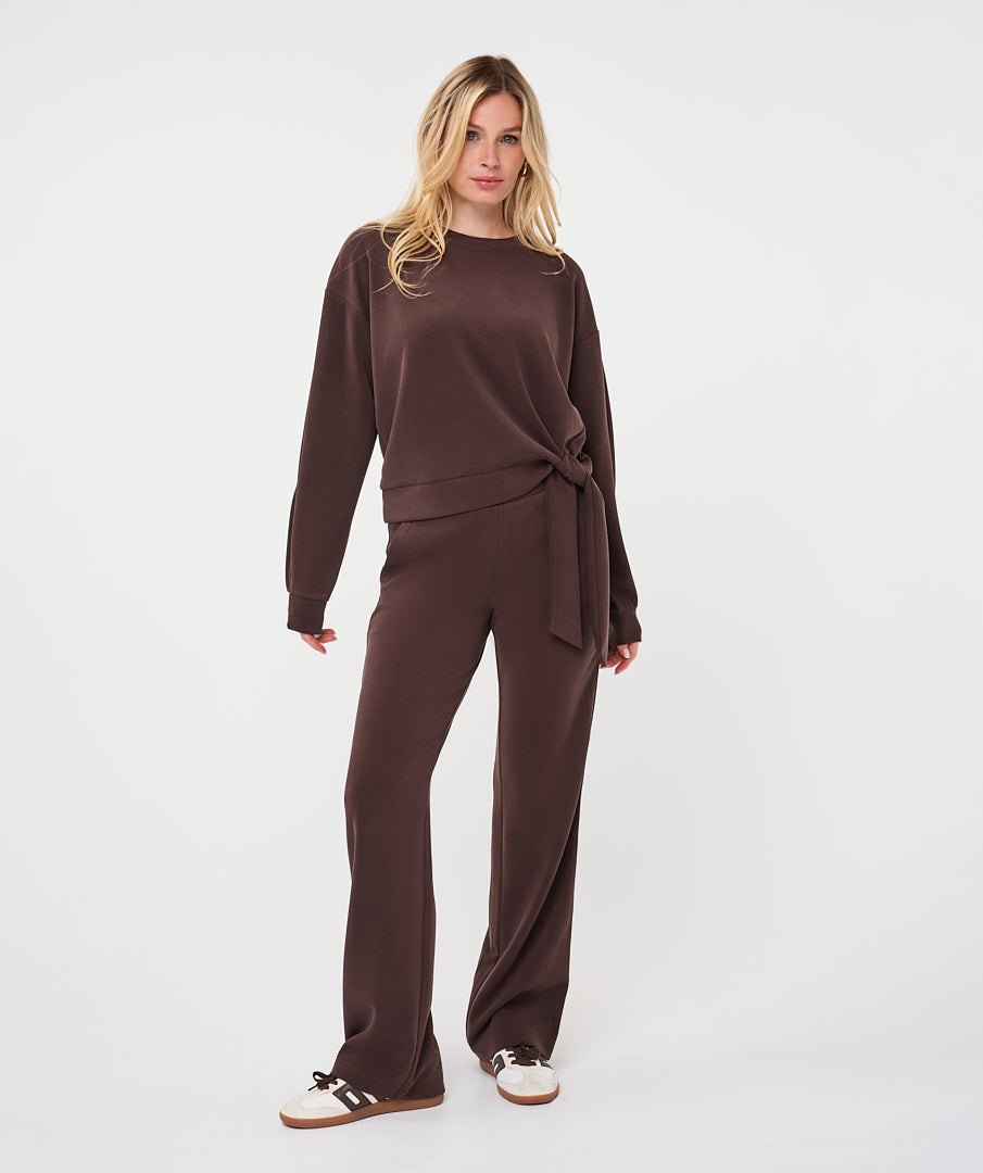 Full-length back view of a woman wearing the chocolate brown Sloane Side-Tie Sweater with matching relaxed-fit trousers, highlighting the coordinated look and fluid drape.