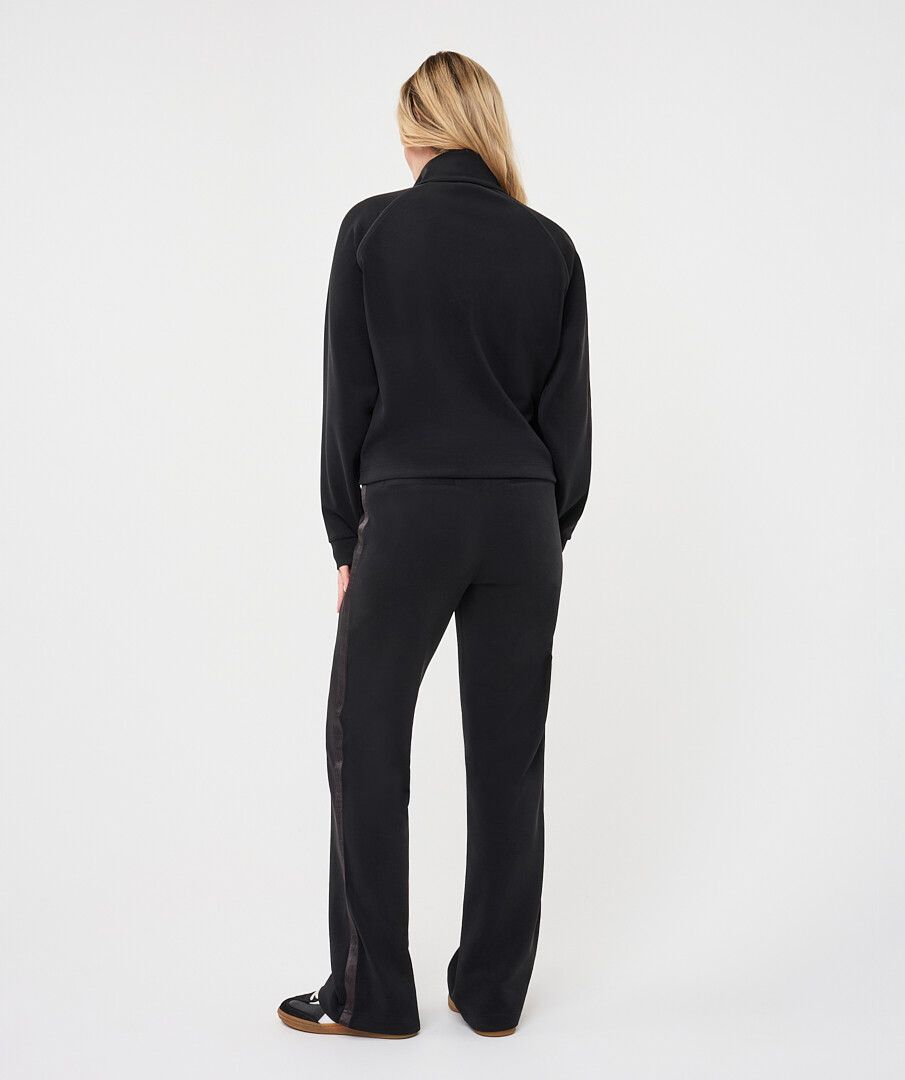 Woman wearing a black utility jacket with a stand collar paired with matching trousers seen from the back.