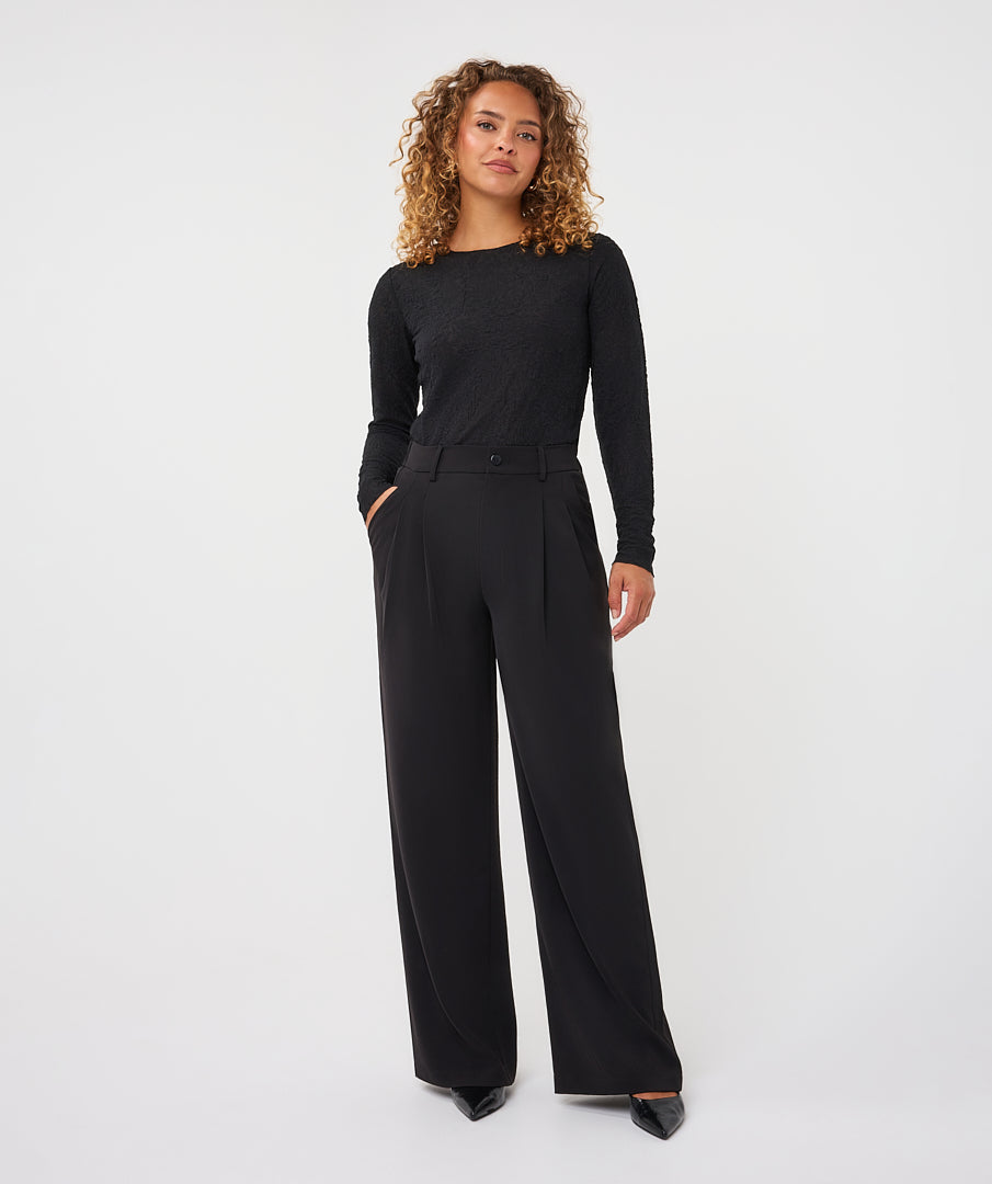 Model wearing black wide-leg trousers with a fitted long-sleeve top and pointed-toe shoes, shown from the front.
