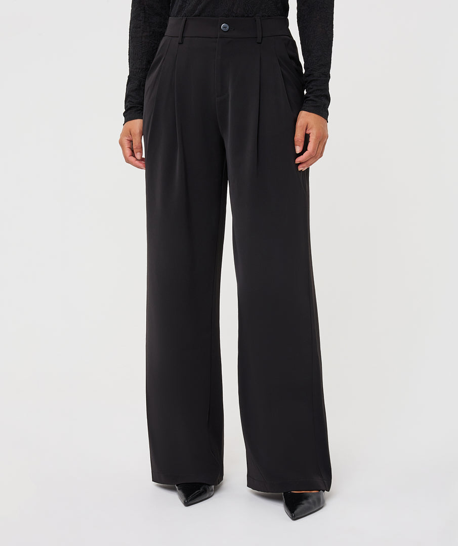 Model wearing black wide-leg trousers with a fitted long-sleeve top and pointed-toe shoes, shown from the front.