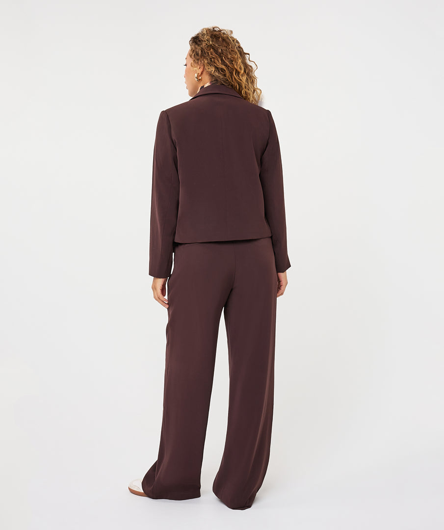 Model wearing a tailored wide-leg trouser suit, shown from the back with a cropped blazer and flowing trousers.