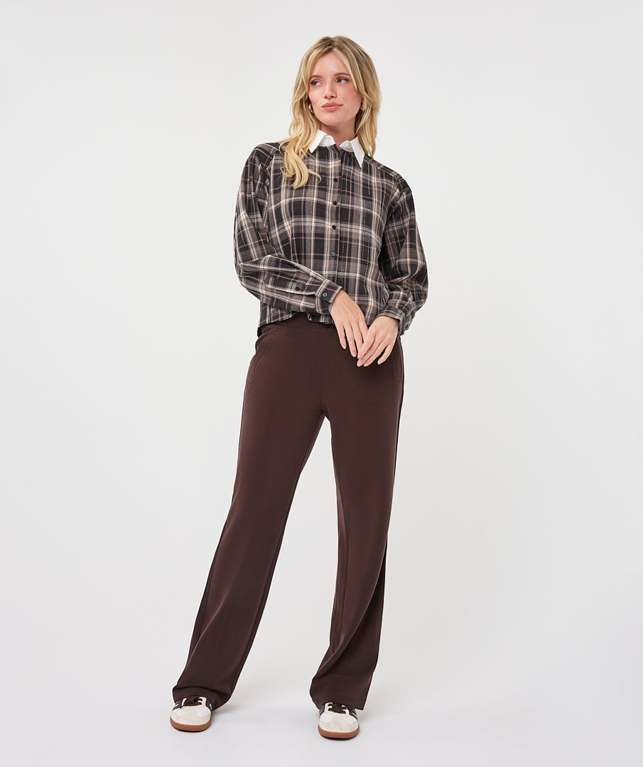 Full-length view of a woman wearing a brown and taupe plaid short blouse with a white collar, paired with wide-leg brown trousers and sneakers.