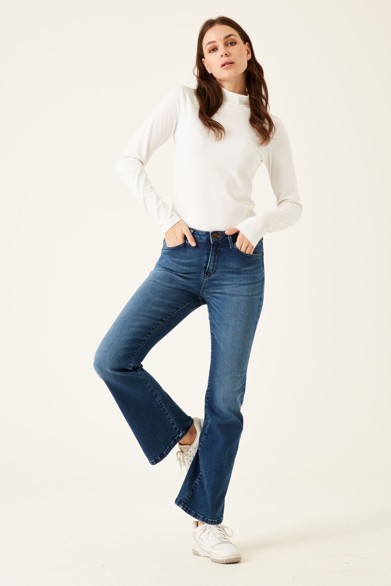 Woman wearing a white turtleneck and blue jeans on a white background