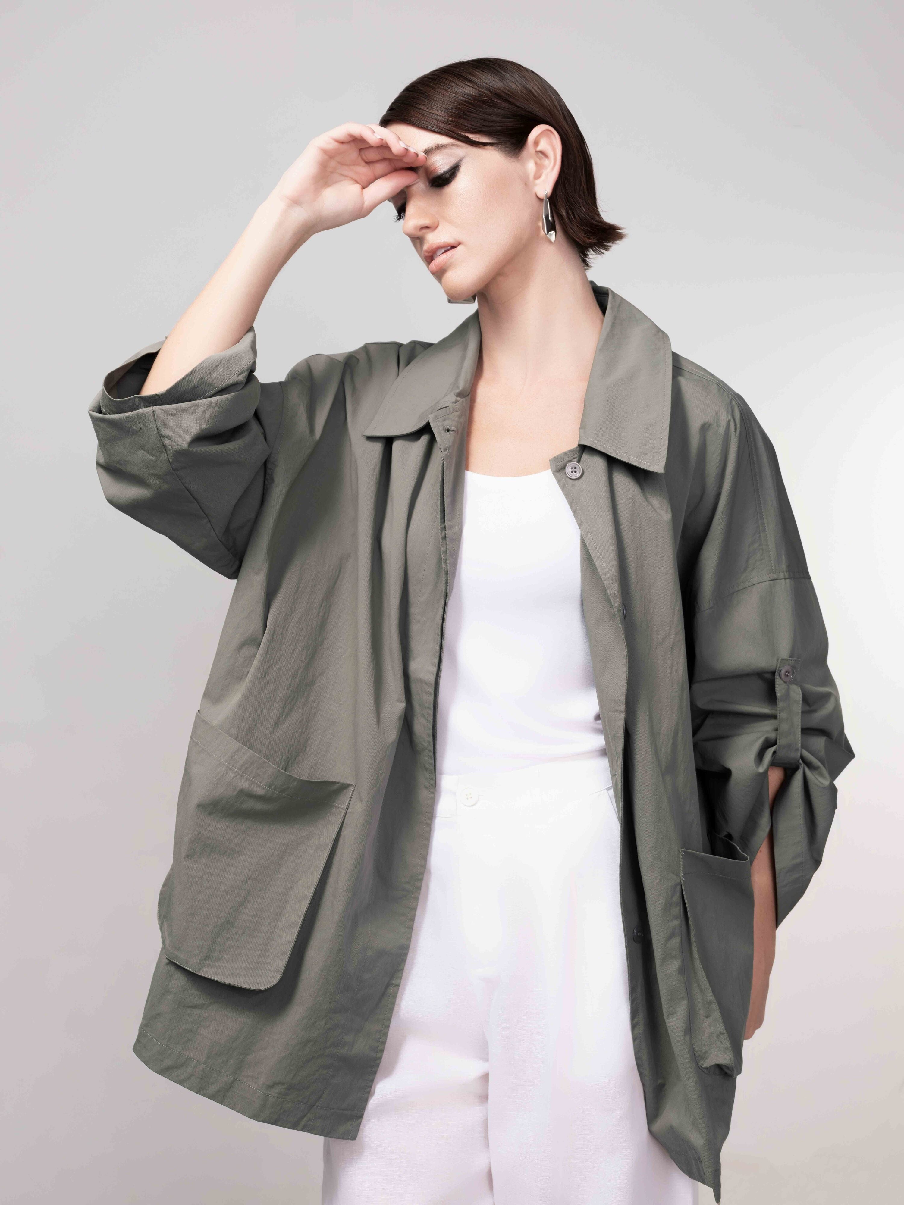 Model in a khaki green relaxed-fit jacket with rolled sleeves, styled over a white top and matching bottoms, posing against a soft grey backdrop.