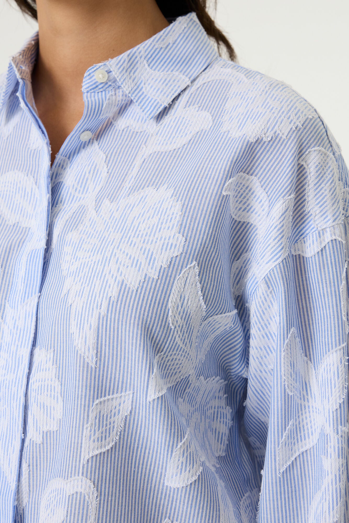 Women's light blue striped cotton blouse with textured floral detailing, featuring a relaxed fit, collared neckline, long sleeves, and button-front closure