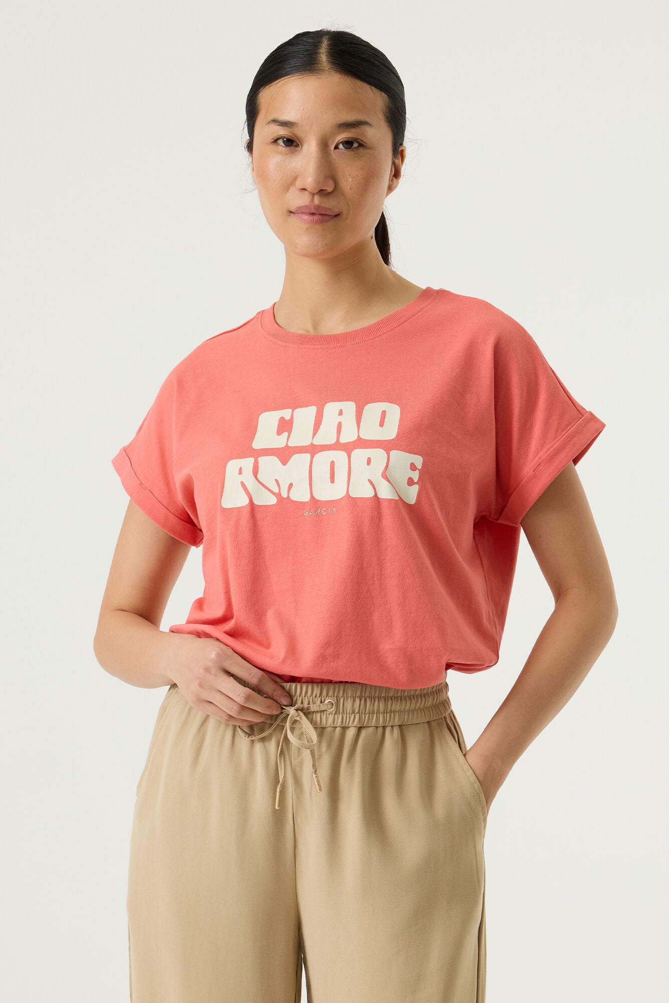 Woman wearing a coral relaxed fit graphic tee with the words Ciao Amore, wide-leg drawstring pants and flat sandals, styled in a casual, comfortable outfit