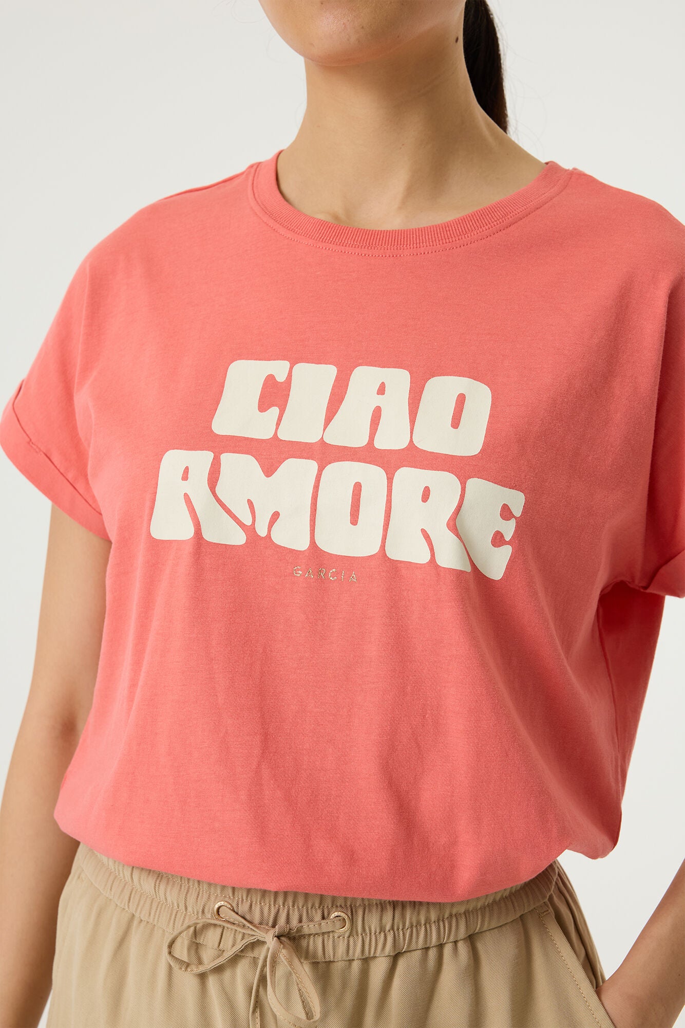 Woman wearing a coral relaxed fit graphic tee with “Ciao Amore” text in light beige, styled with beige wide-leg drawstring pants