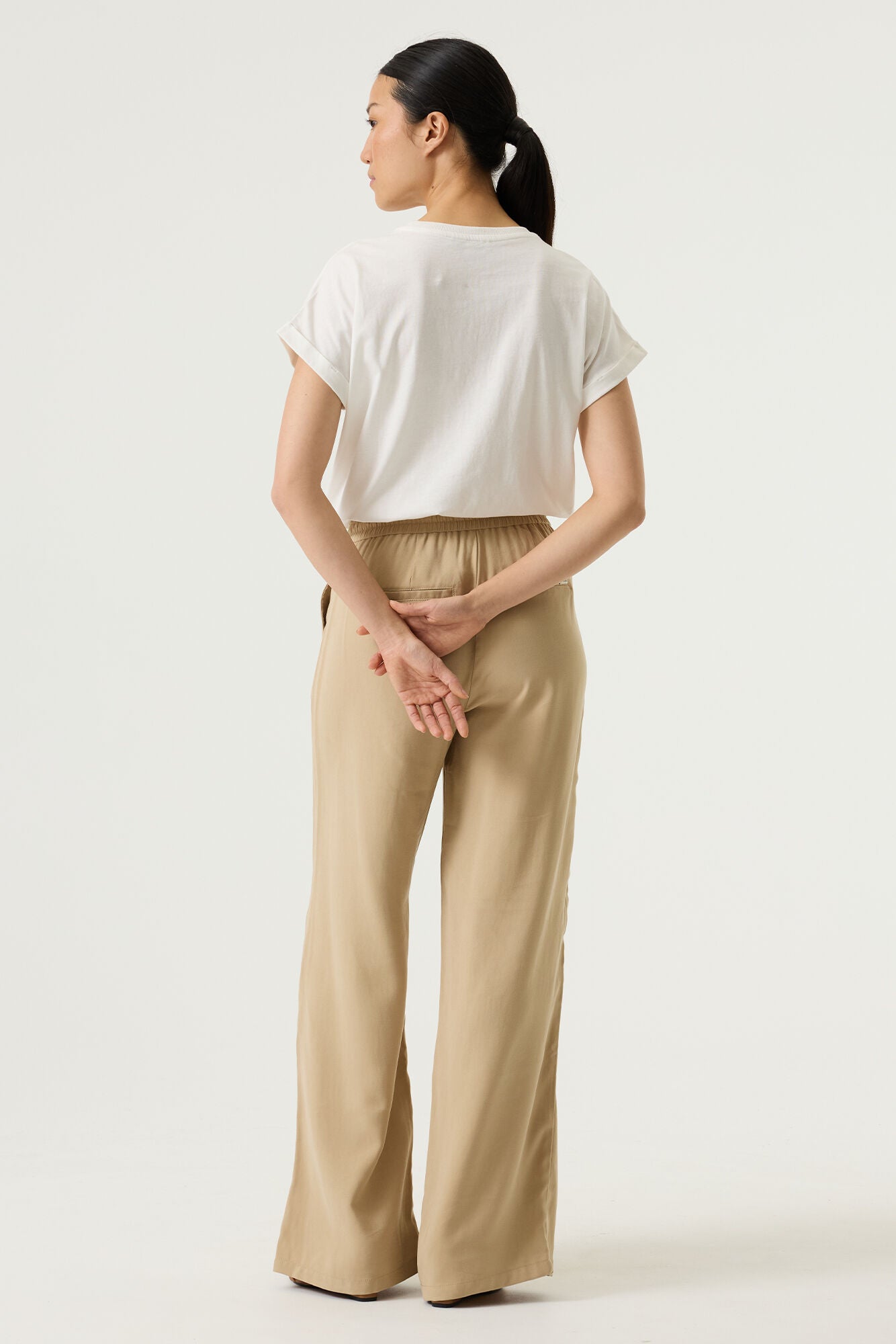 Woman wearing a white relaxed fit graphic tee with “Ciao Amore” text in pink, paired with beige wide-leg drawstring pants and flat sandals