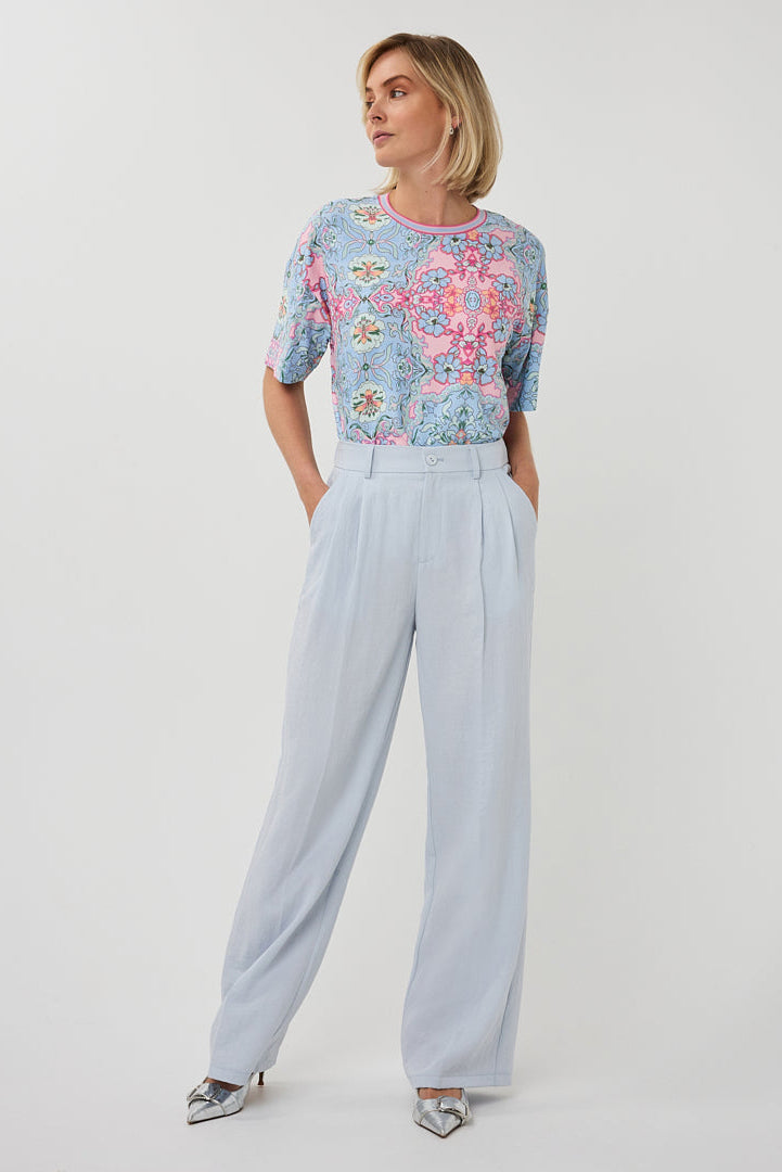 Woman wearing a floral top and light blue pants on a white background