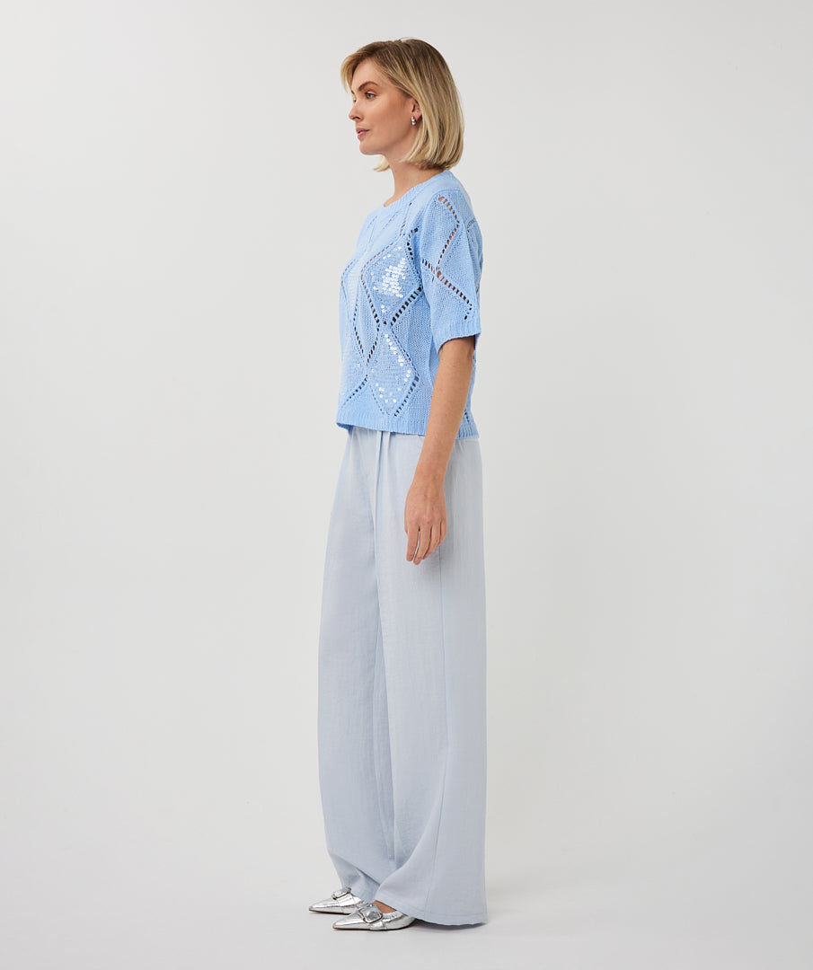 Woman wearing a light blue short-sleeve pointelle knit sweater with subtle sequin detailing, styled in a relaxed fit with a crew neckline.