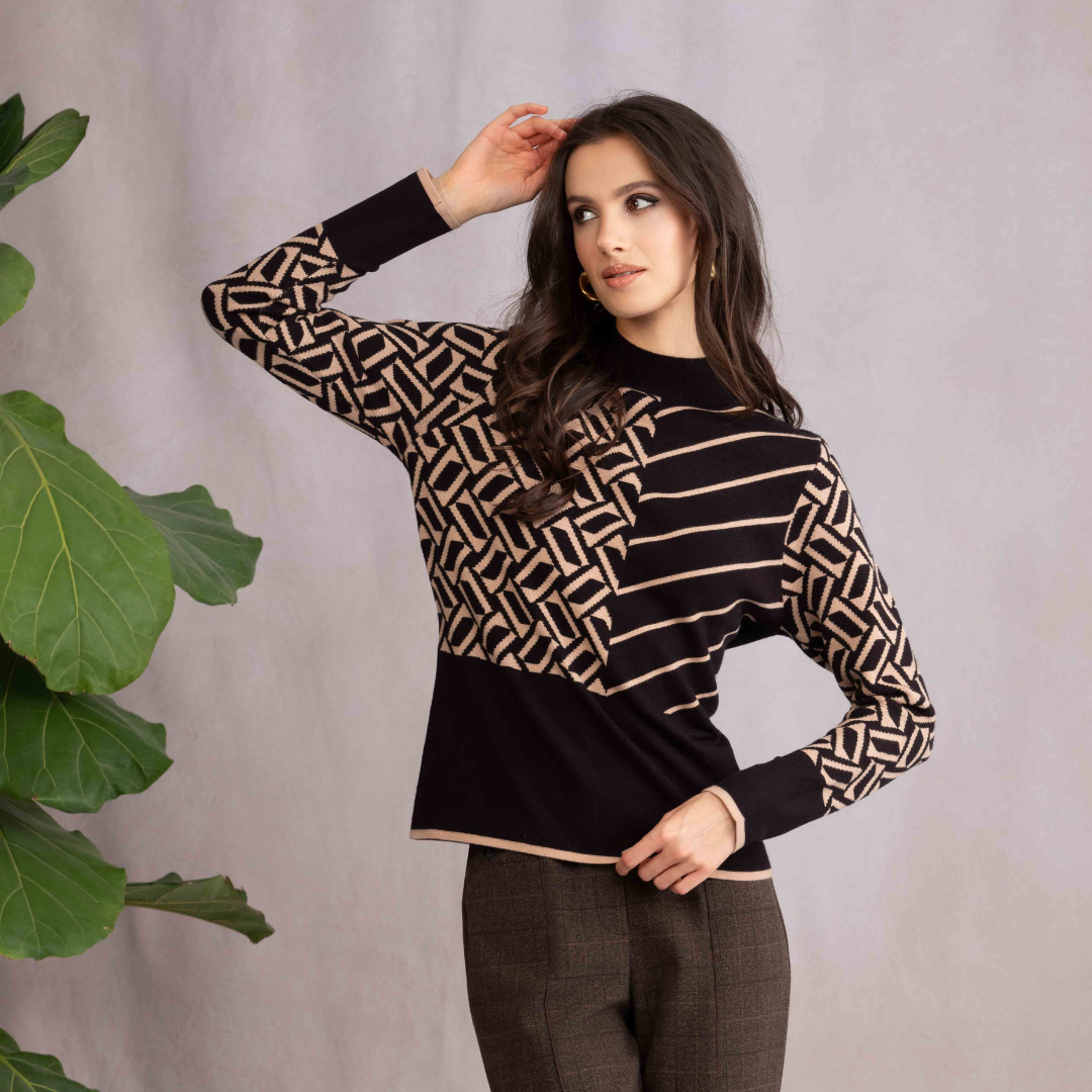 Woman wearing a black and gold patterned sweater with brown pants against a neutral background