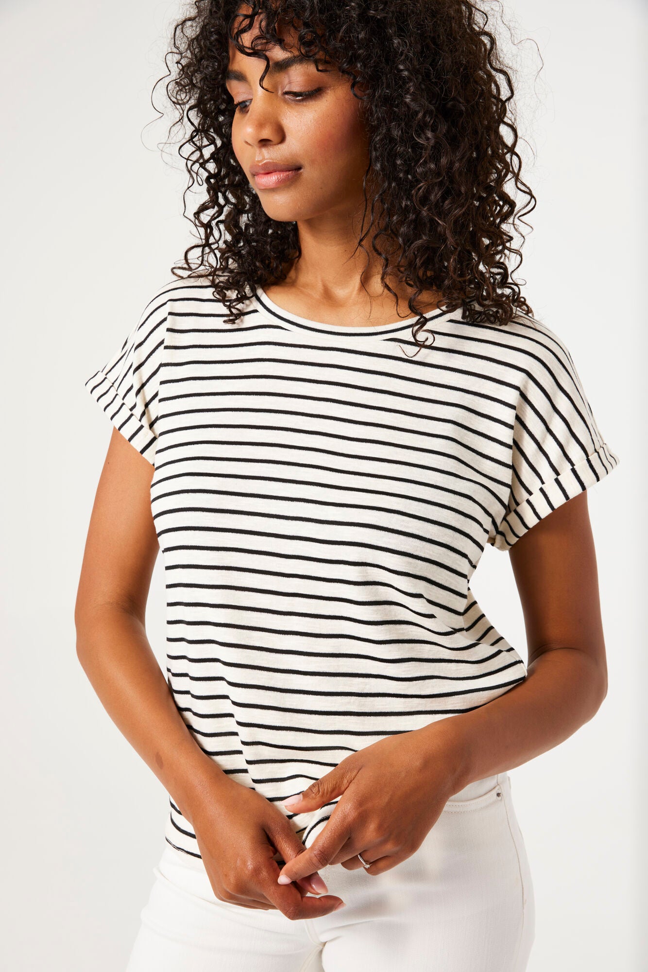 Women's black and white striped knit t-shirt featuring a relaxed silhouette, rolled short sleeves, and round neckline. Paired with grey slim-leg jeans and chunky sneakers.