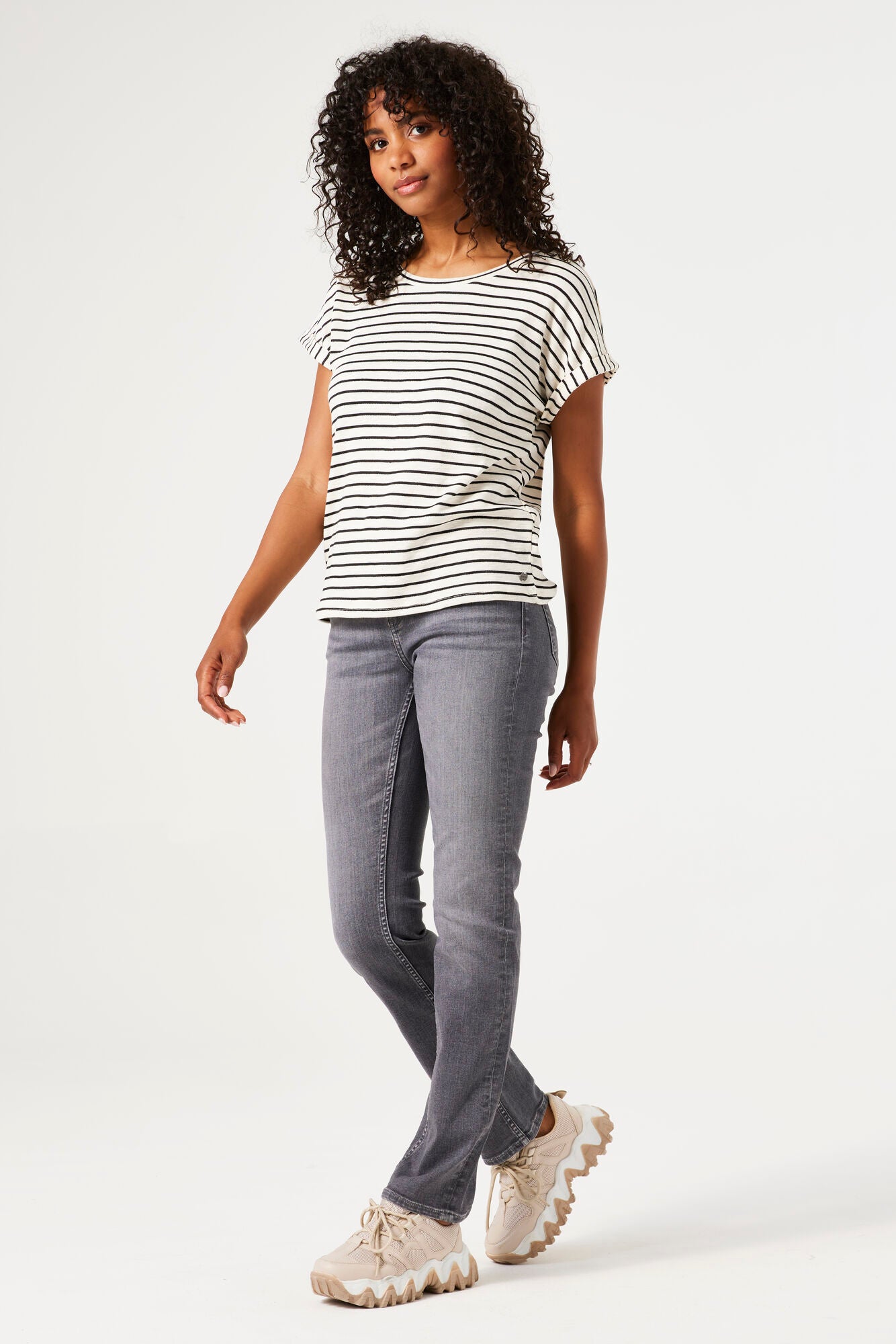 Women's black and white striped knit t-shirt featuring a relaxed silhouette, rolled short sleeves, and round neckline. Paired with grey slim-leg jeans and chunky sneakers.