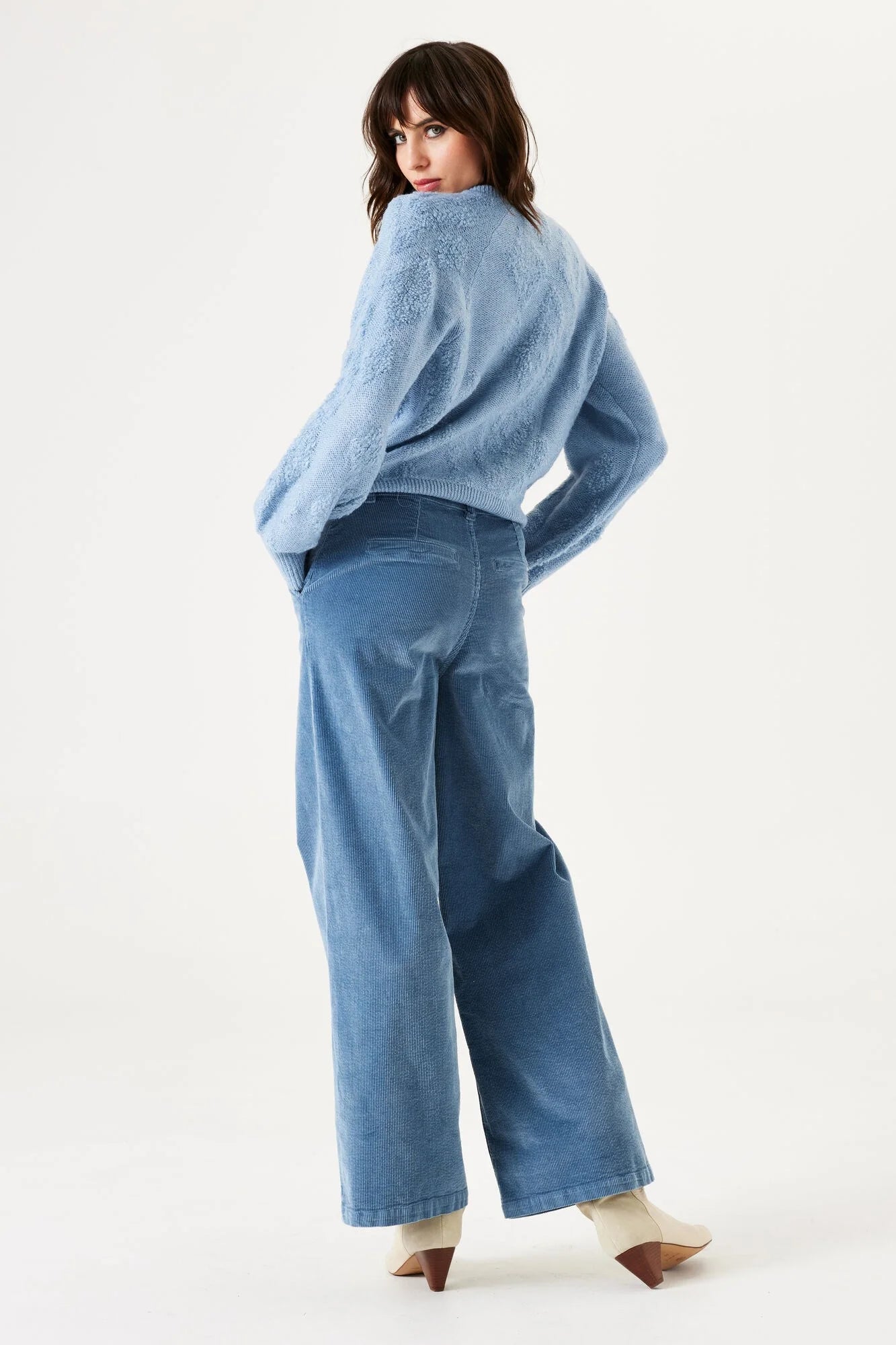 Woman wearing a light blue sweater and dark blue pants on a white background