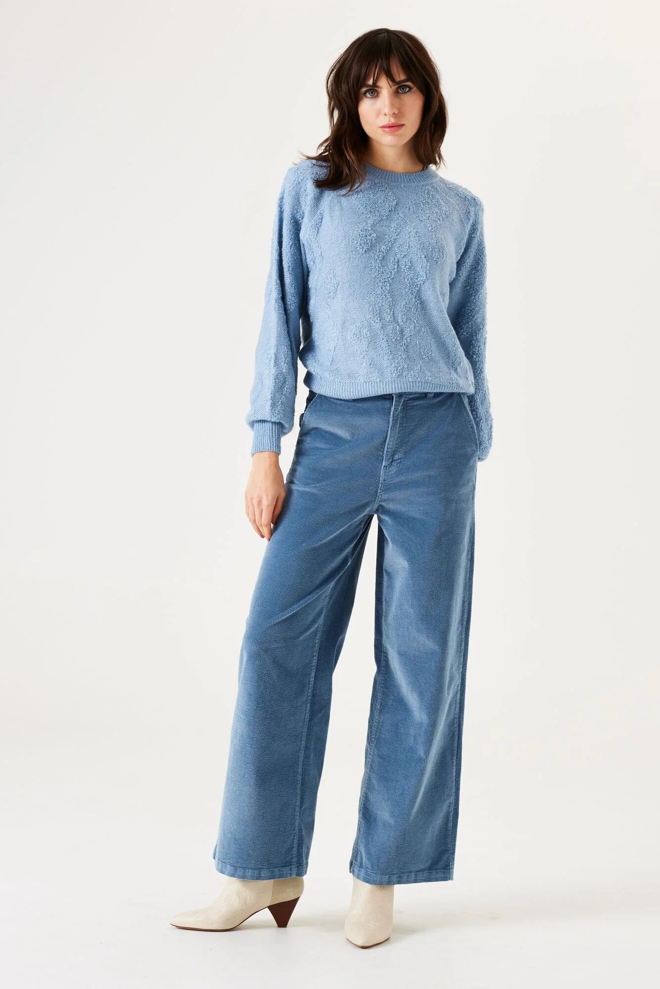 Woman wearing a light blue sweater and jeans on a white background