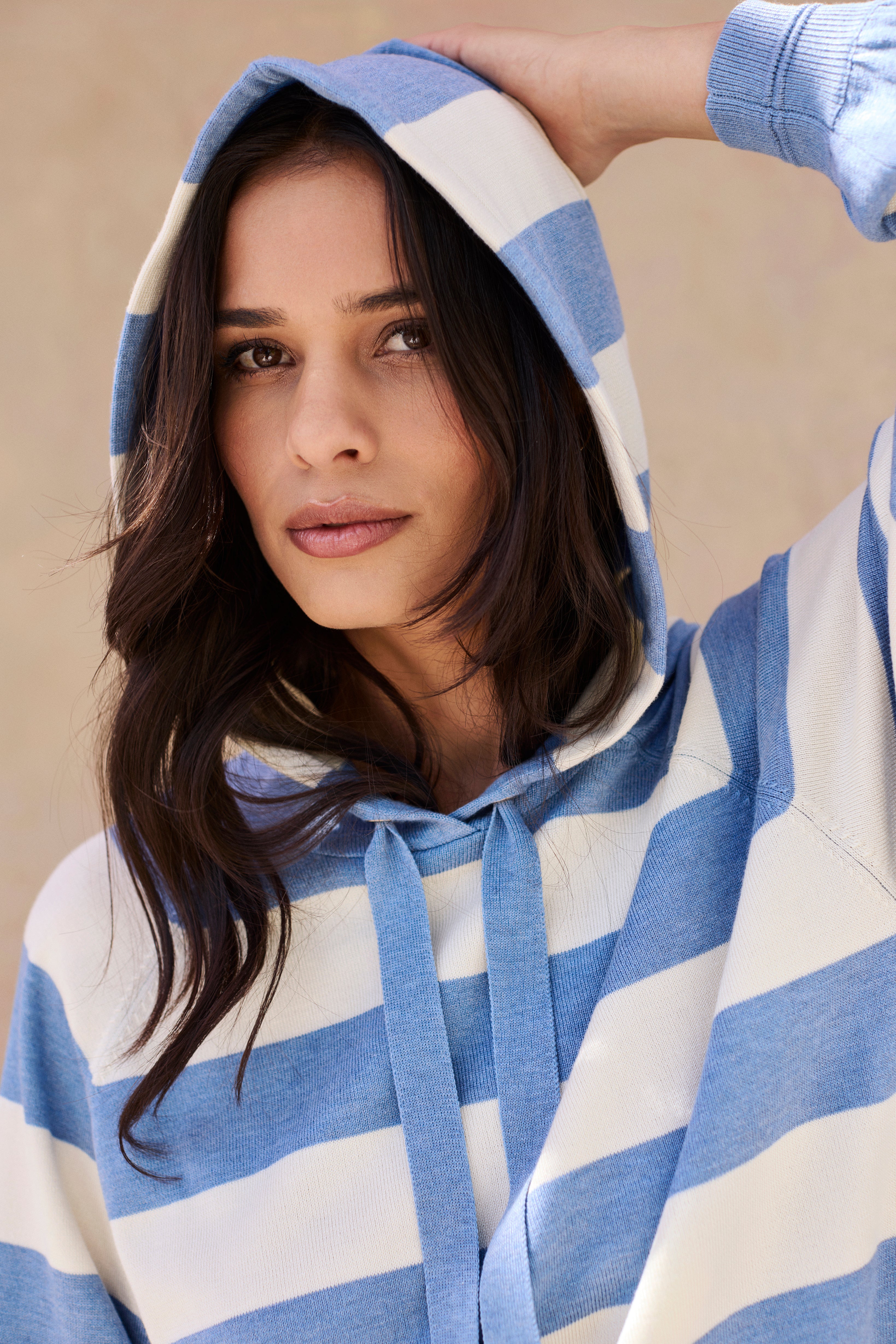 Woman wearing a blue and white striped hoodie against a beige background