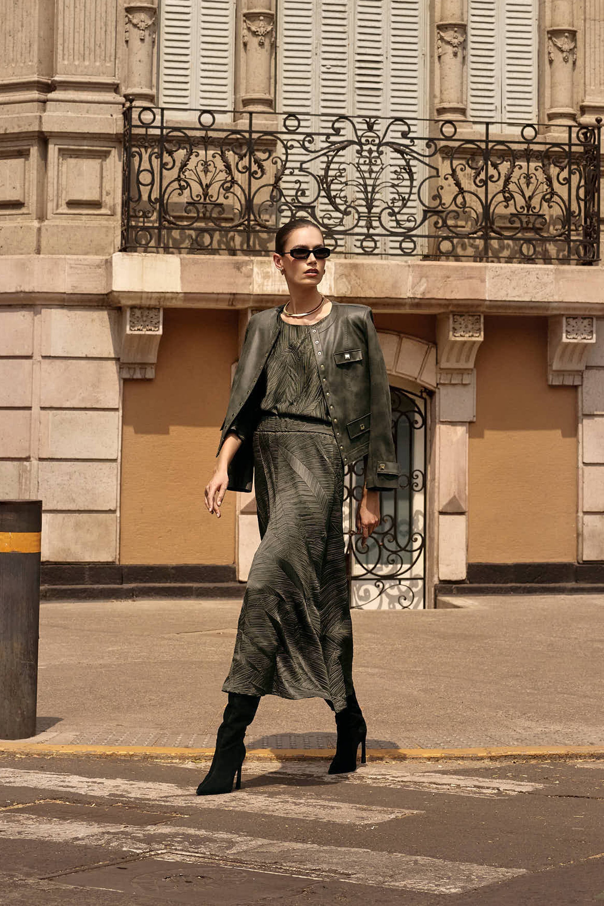 woman crossing the street wearing a fashionable green outfit