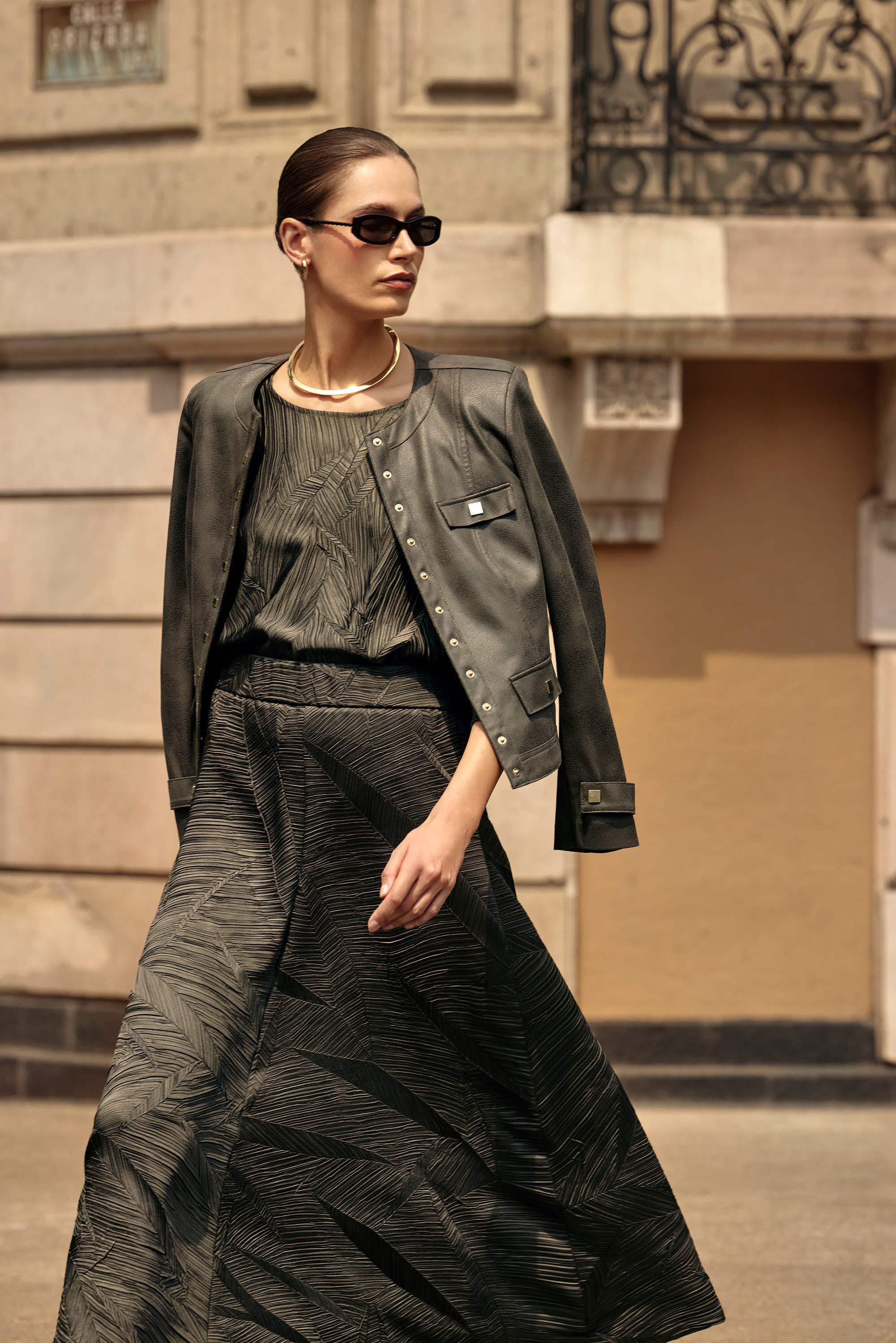 woman crossing the street in a dark green outfit and sunglasses