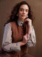 Woman wearing a brown knit button-front vest over a brown-and-white striped long-sleeve blouse, styled with coordinating striped trousers, featuring gold-tone buttons and patch pockets.