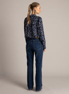 Back view of a navy printed blouse with gathered yoke and blouson sleeves, paired with dark wash jeans.