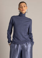 Woman wearing a blue sparkle turtleneck sweater with metallic wide-leg trousers.