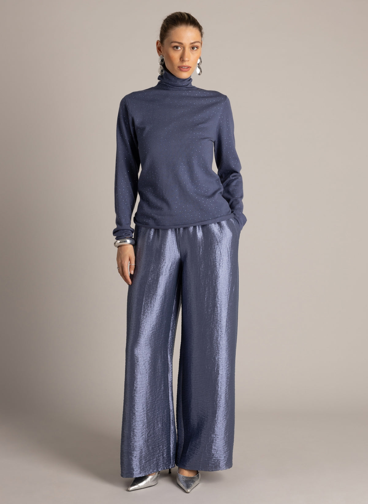 Full-length front view of a blue sparkle turtleneck sweater paired with metallic wide-leg trousers and silver heels.