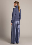 Back view of a blue sparkle turtleneck sweater styled with shimmering metallic wide-leg pants.