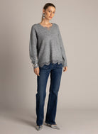Full-length front view of a grey lace-trim V-neck sweater styled with dark flared jeans and silver heels.