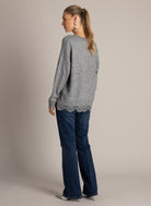 Back view of a grey sweater showing the relaxed silhouette and lace trim peeking out along the hem, paired with denim.