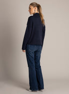Back view of a navy blue sweater showing the ribbed mock neckline, dropped shoulders, and relaxed boxy fit, paired with flared denim.