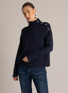 Woman wearing a navy blue button-shoulder sweater with a ribbed mock neckline, styled with dark wash flared jeans.