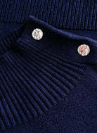 Close-up of navy sweater's silver decorative buttons and ribbed shoulder seam detail on a chenille-like knit texture.