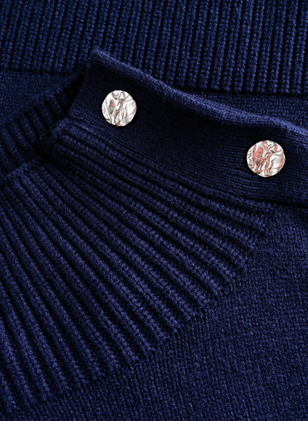 Close-up of navy sweater's silver decorative buttons and ribbed shoulder seam detail on a chenille-like knit texture.