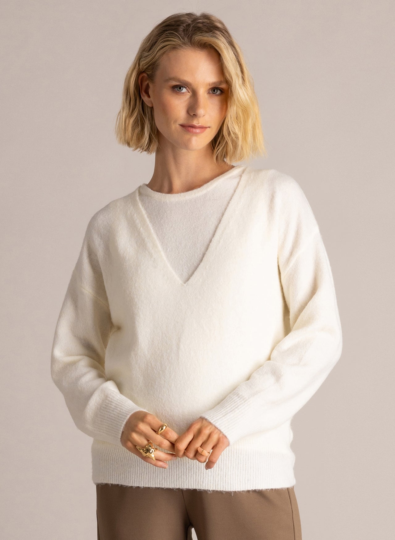 Woman modelling an ivory V-neck layered sweater with long sleeves and ribbed trim, paired with brown wide-leg trousers.