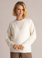 Woman modelling an ivory V-neck layered sweater with long sleeves and ribbed trim, paired with brown wide-leg trousers.