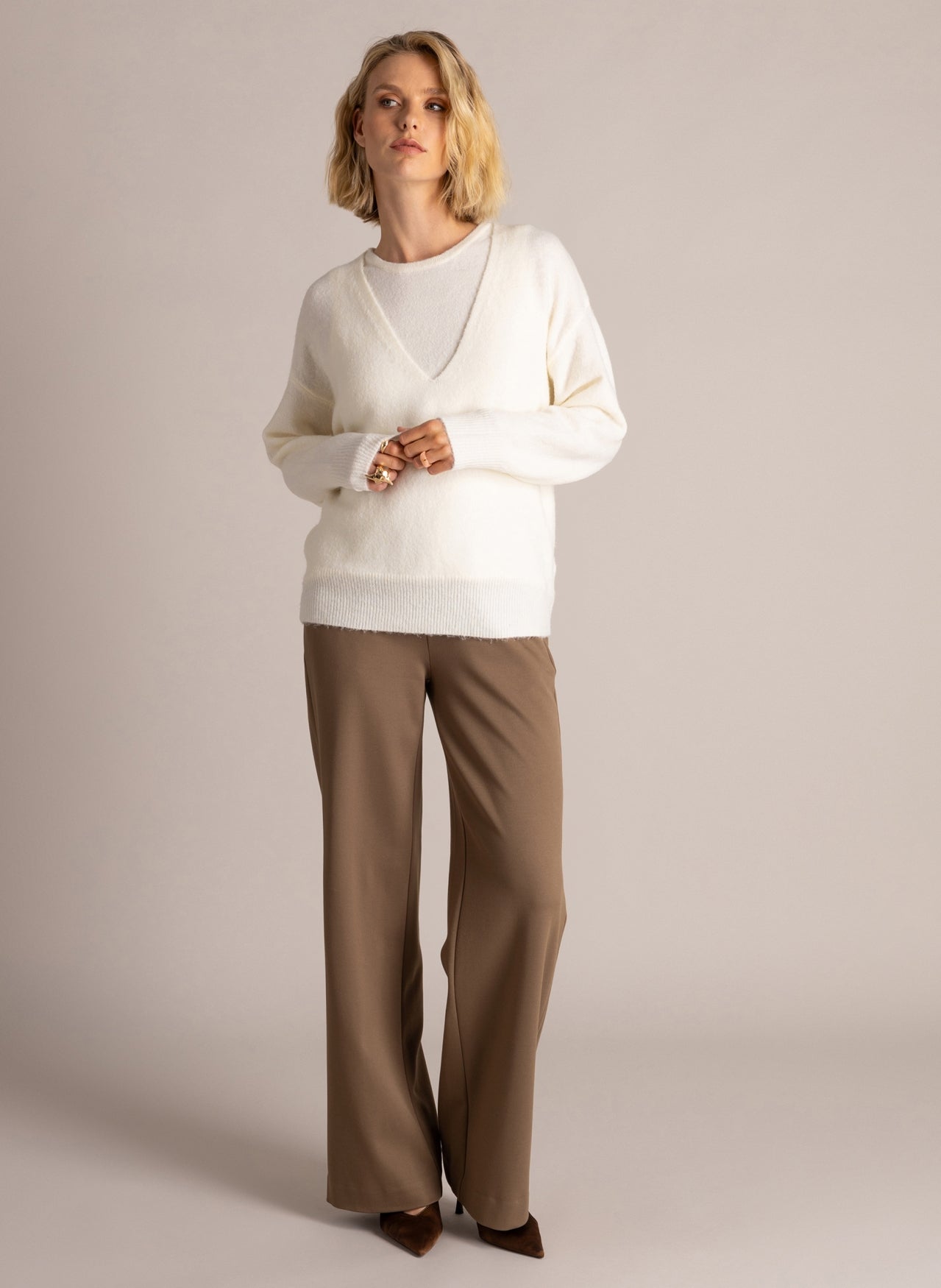 Full-length woman modelling an ivory V-neck layered sweater with long sleeves and brown wide-leg trousers, styled with brown pointed-toe heels.